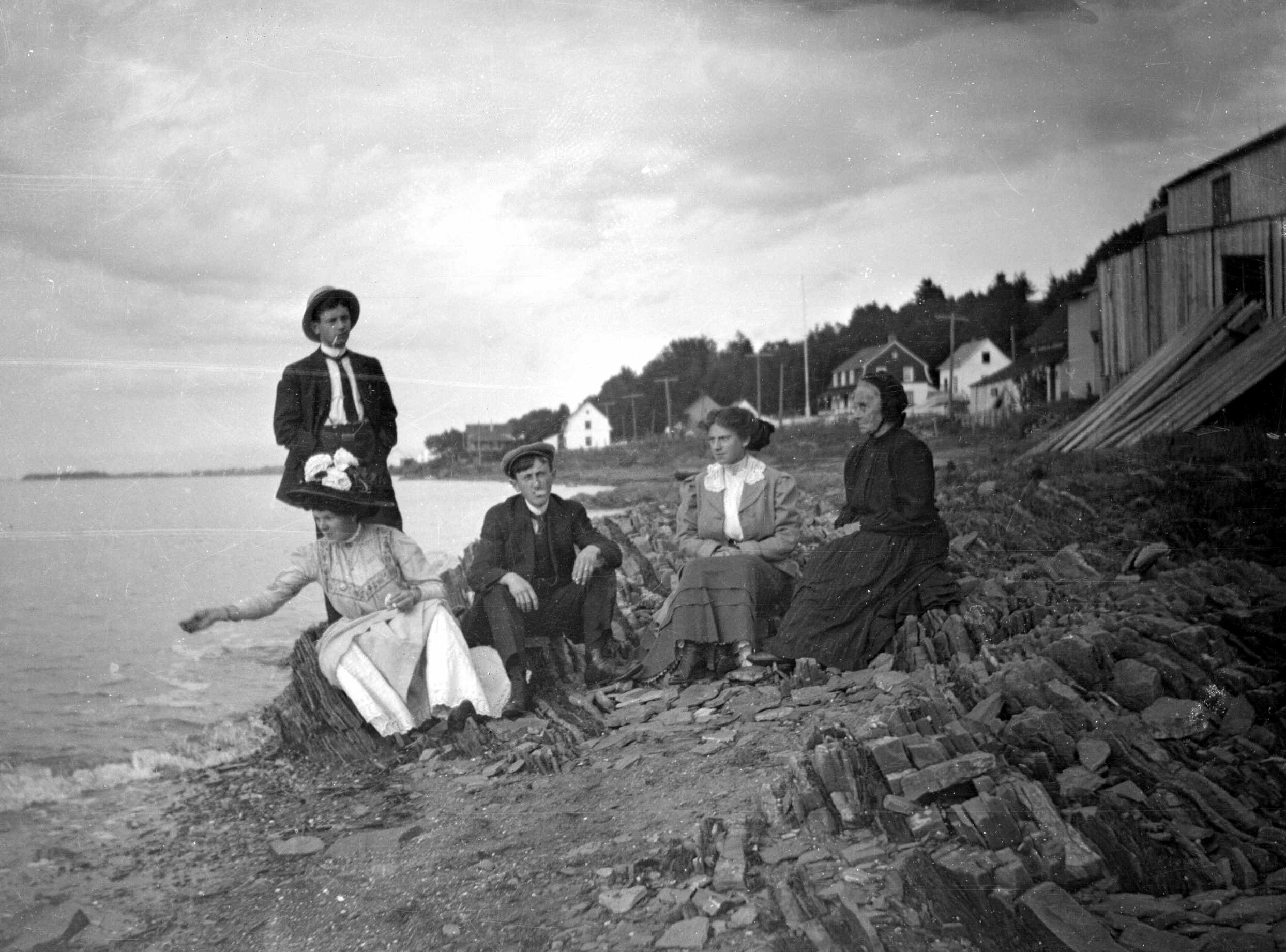 Cinq adultes, dont une dame âgée, posent sur une plage très rocheuse. Une femme semble lancer du pain à un oiseau hors champ.