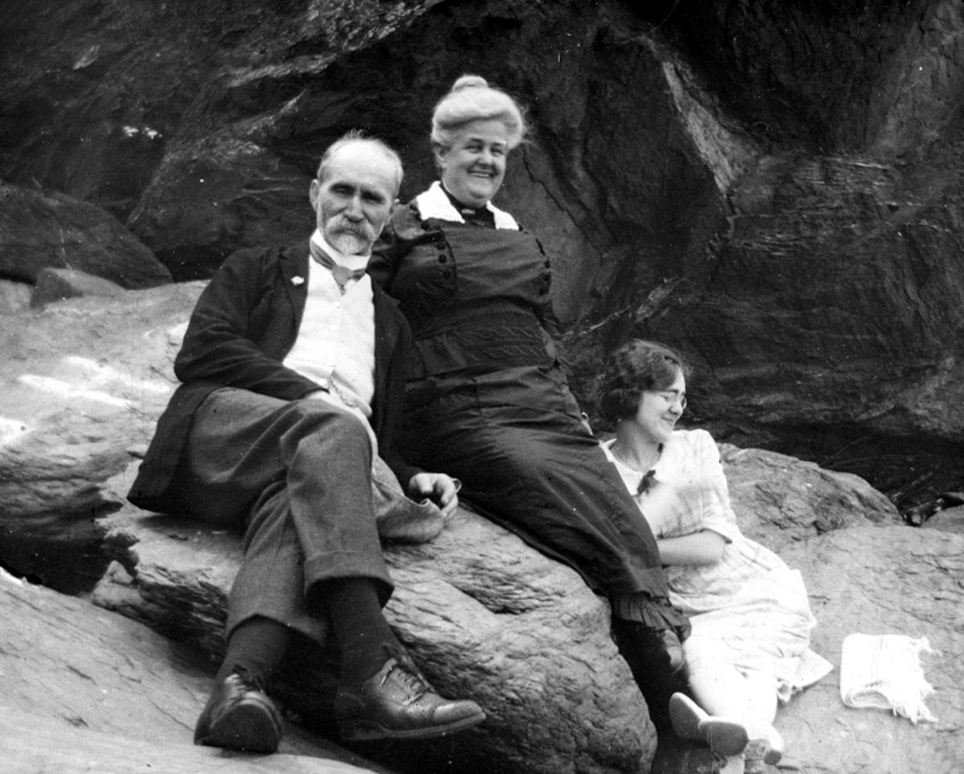 Des adultes plutôt distingués (un couple d’âge mûr et une jeune fille) sont assis sur un rocher, détendus et souriants.